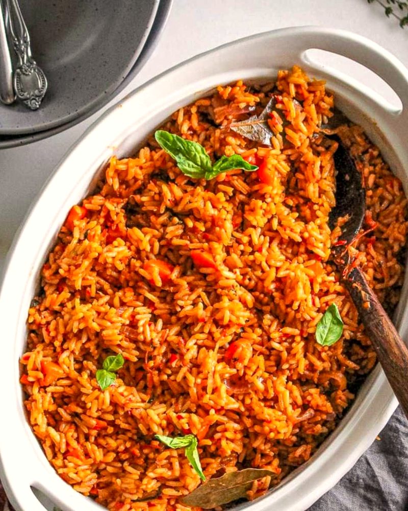 A bowl of deep red jollof rice with a wooden spoon