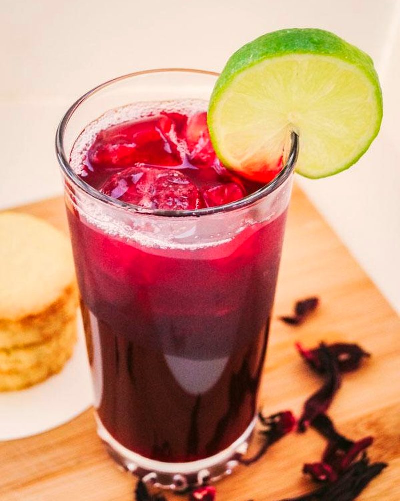 A tall glass of deep red zobo with lime and dried hibiscus petals